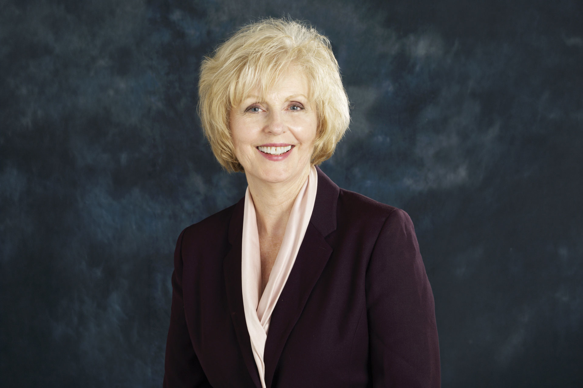 Linda Clark smiling professionally in a dark blazer with a white scarf against a neutral background.