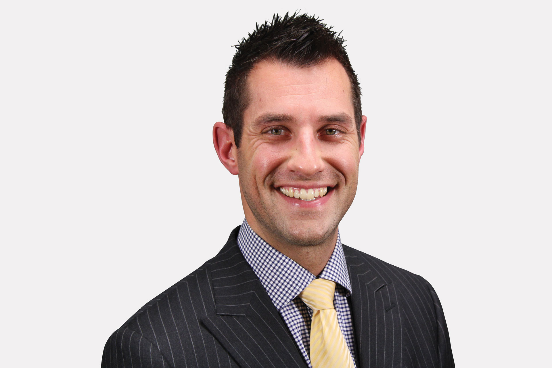 Lucas Gafken smiling professionally in a dark suit with a checked shirt and yellow tie against a neutral background as a speaker for Apex Seminars.