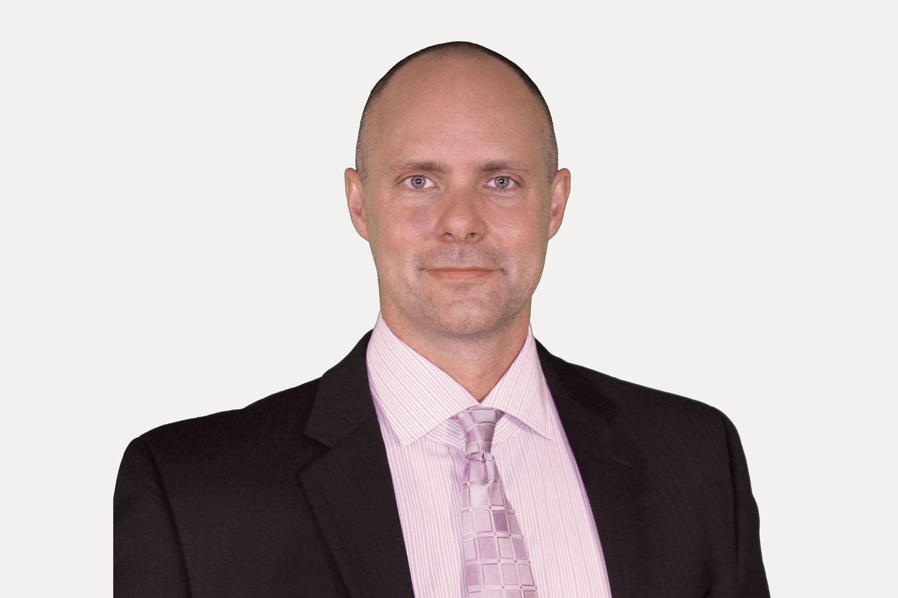 Steven Noseworthy smiling professionally in a dark suit with a white shirt and patterned pink tie against a neutral background.
